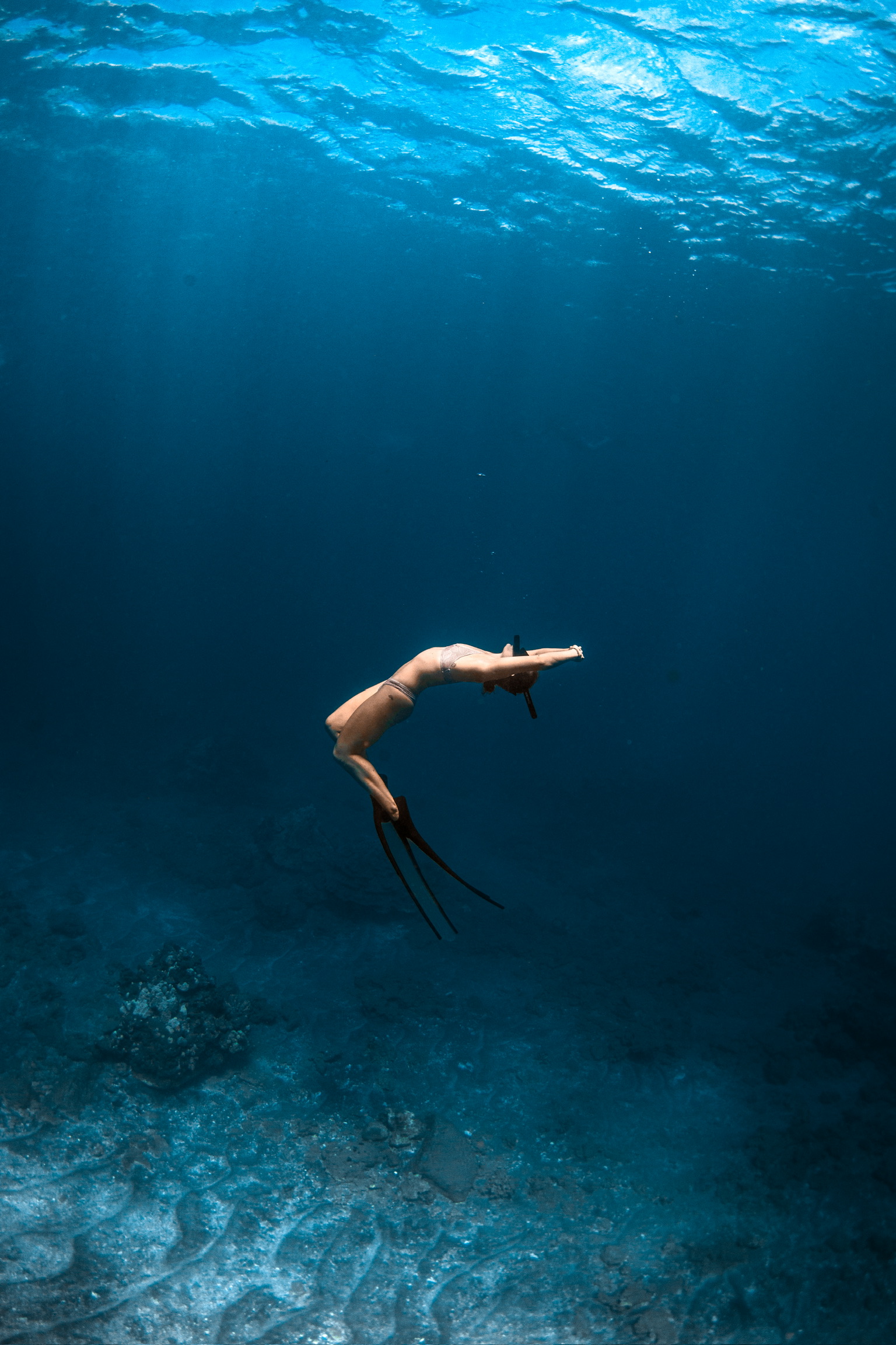 A freediver arcing downward into deep blue water